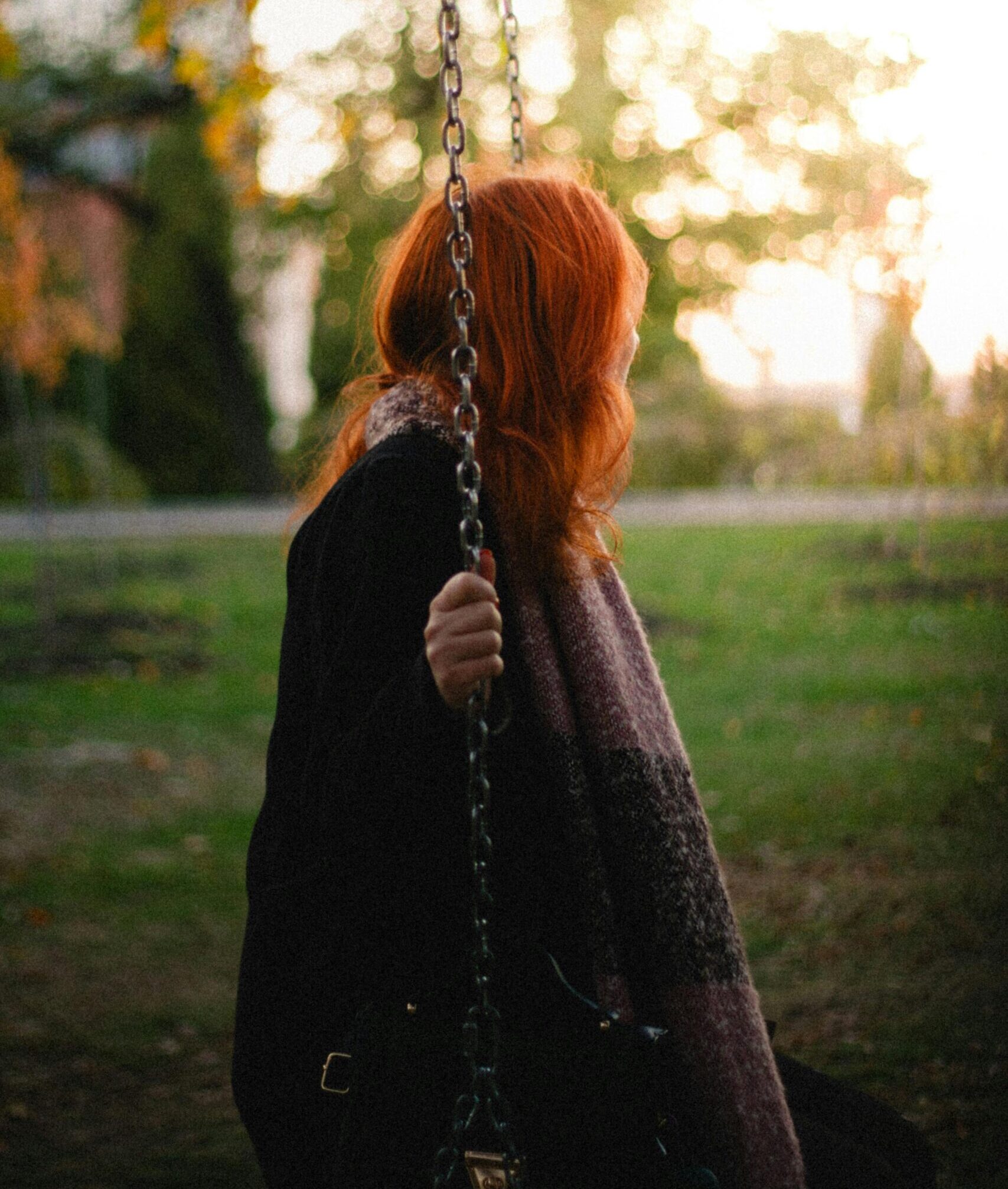 A woman with red hair on a swing in a serene autumn park setting.