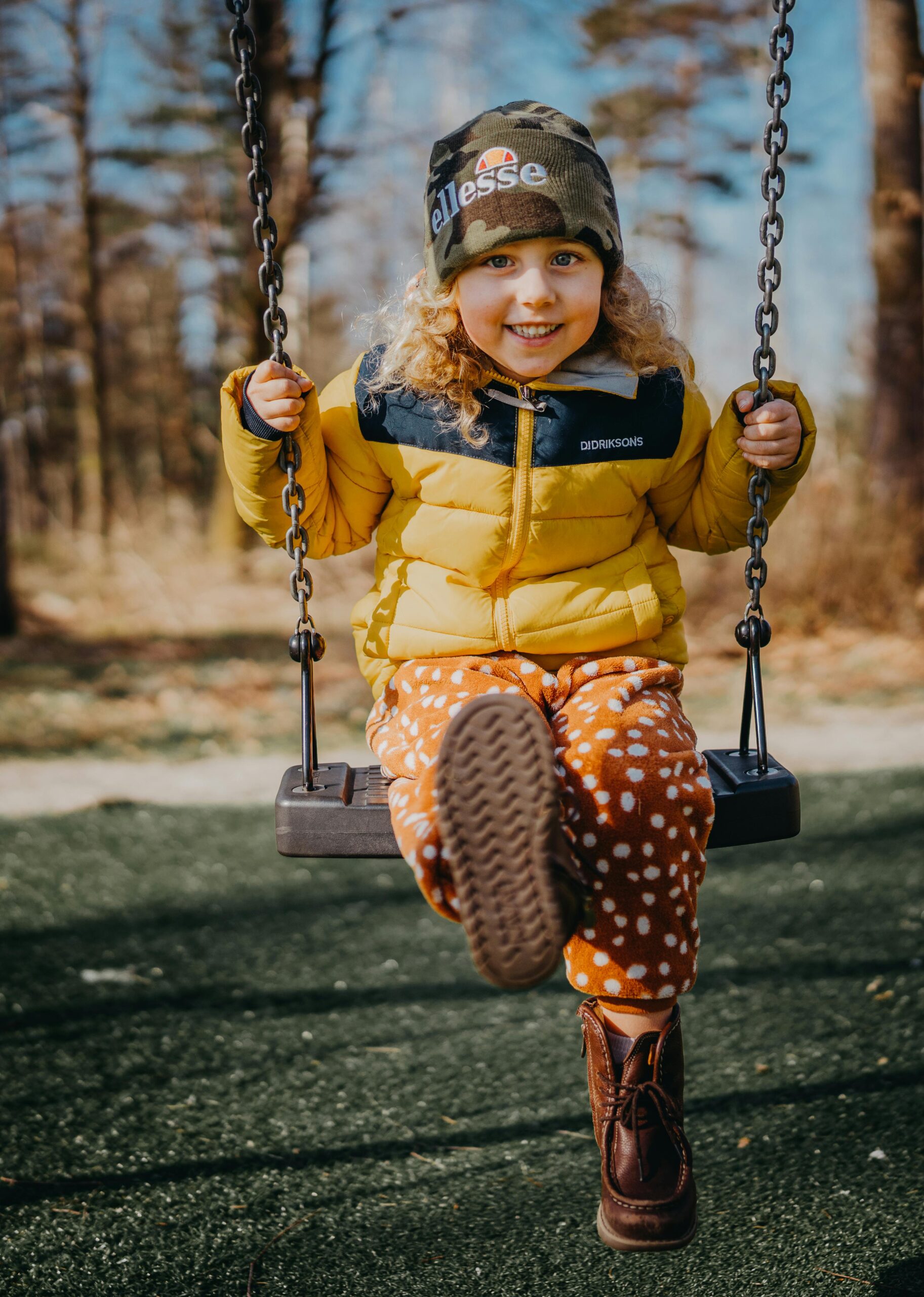 Smiling child in yellow jacket swinging outdoors. Bright autumn day with happiness and play.