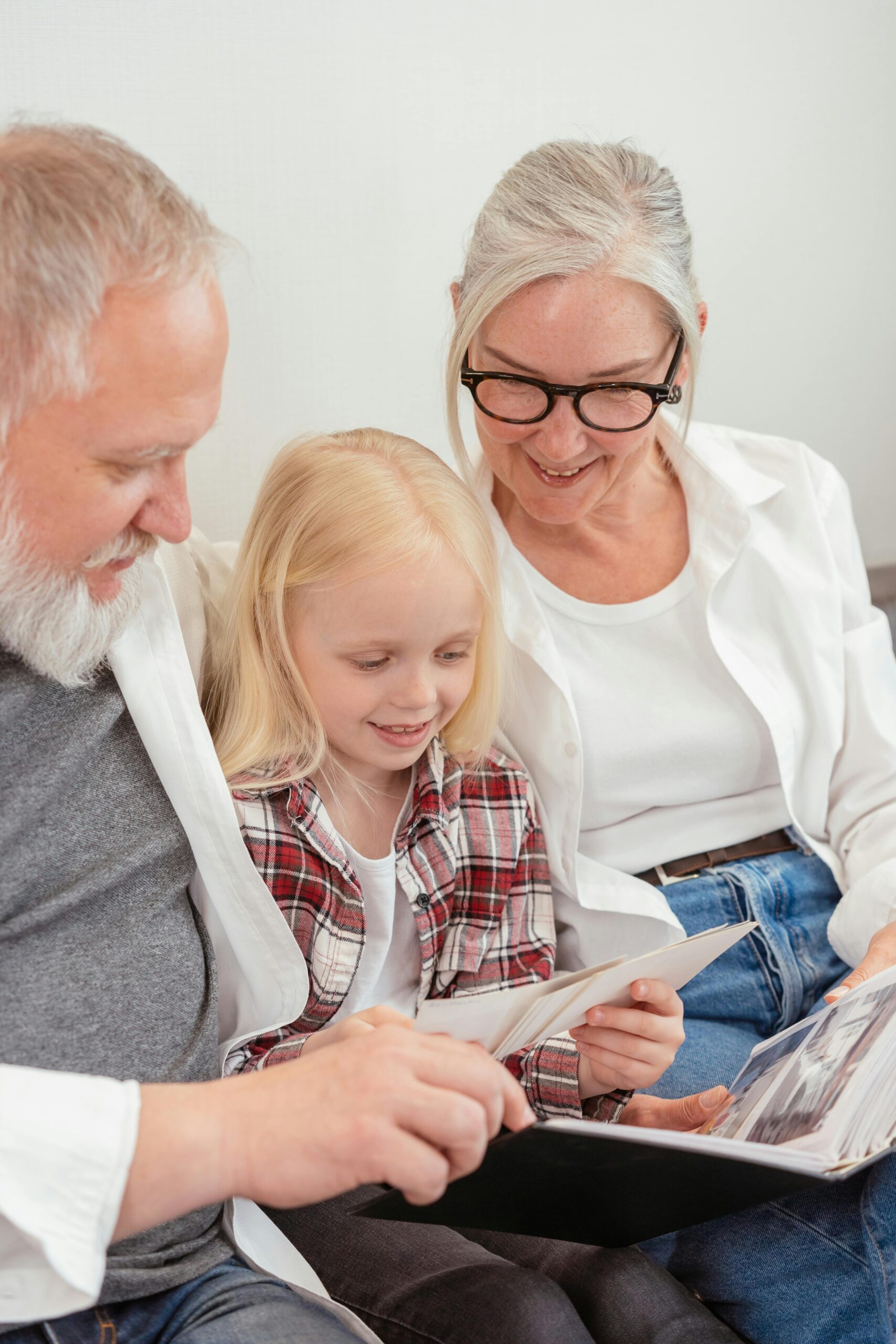 Elderly couple and young girl enjoying family photo album at home.